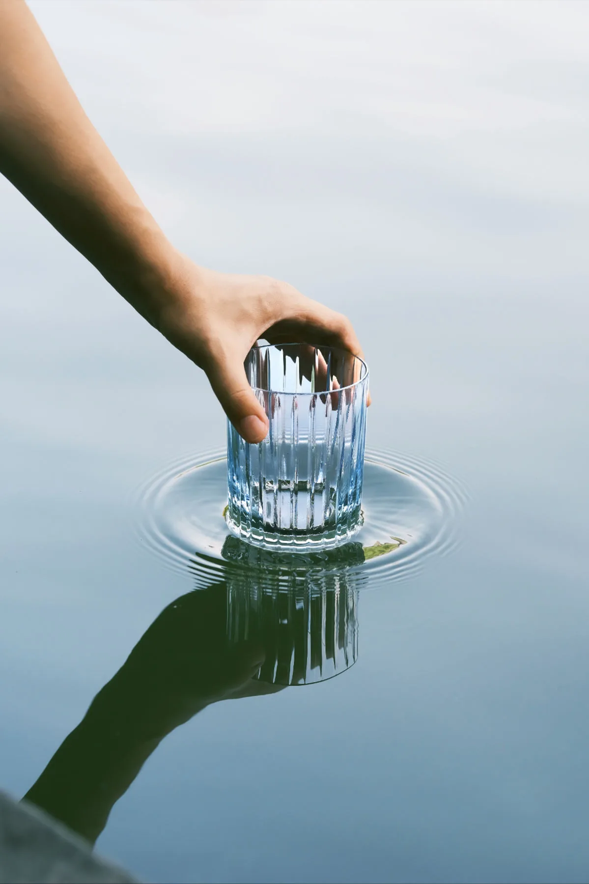 Mano que sostiene un vaso de cristal sobre la superficie del agua