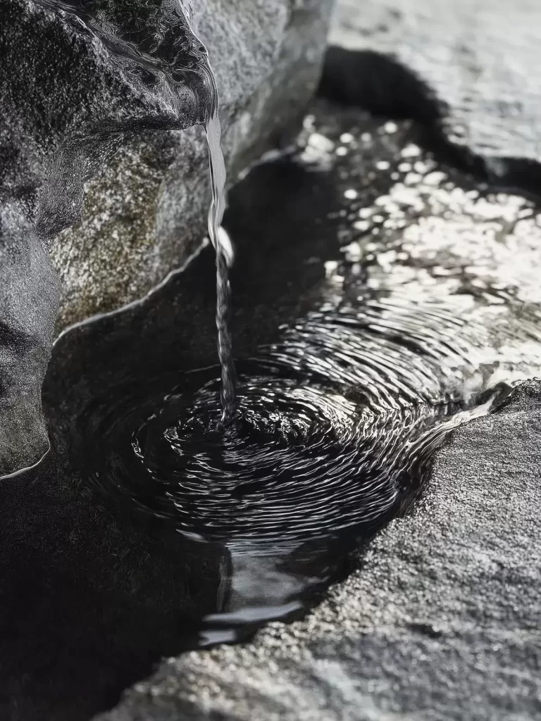 Hilo de agua que brota entre rocas volcánicas y forma un pequeño remanso
