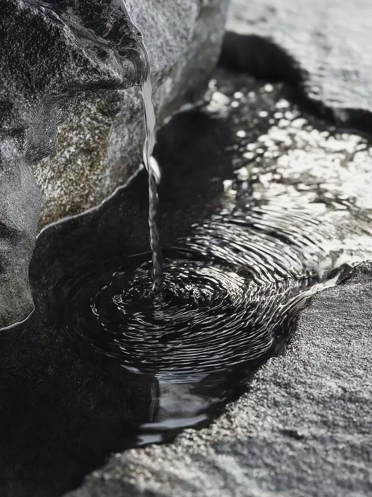 Hilo de agua que brota entre rocas volcánicas y forma un pequeño remanso