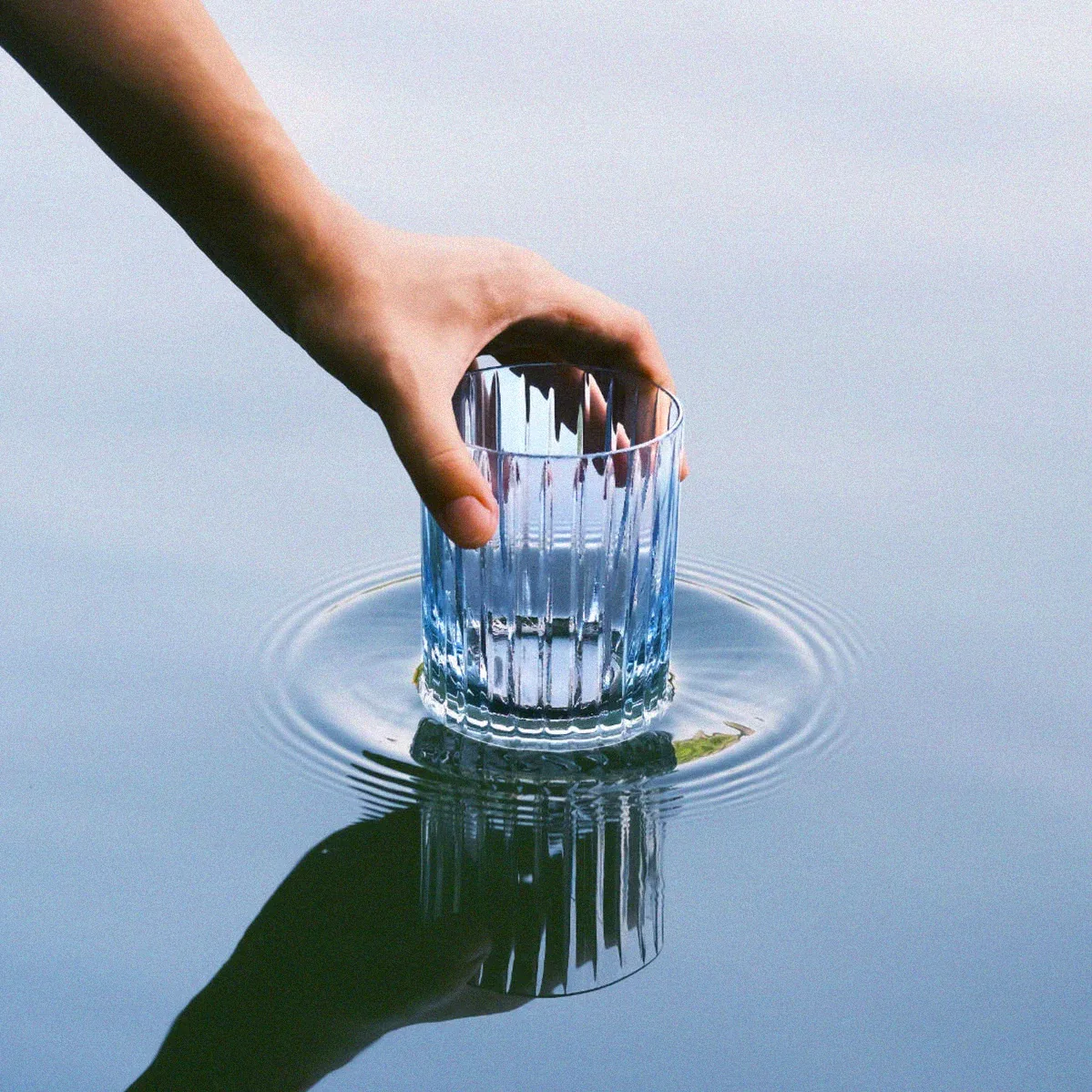 Mano posando un vaso de agua sobre una lámina de agua en calma