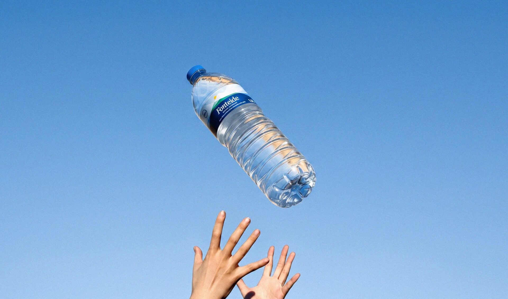 Botella de agua mineral natural Fonteide lanzada al cielo azul sobre dos manos